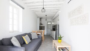 Una sala de estar moderna y luminosa con un sofá gris, una mesa de comedor de madera y una cocina al fondo.