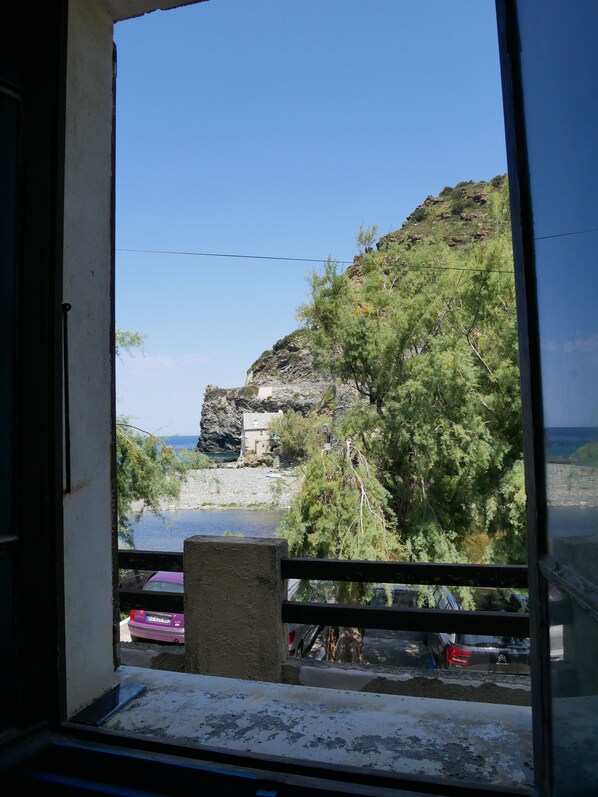 A view from a window overlooking a rocky coastline with a building on the shore and a clear sky.