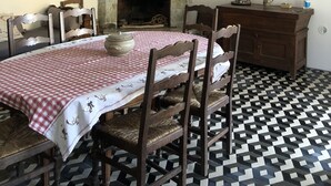 Ein Esszimmer mit kariertem Tischläufer, Holzsesseln, einem Kamin und einer Pendelleuchte.