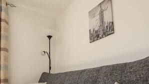 A grey sofa with two cushions, a remote control on it, and a lamp with a single bulb.