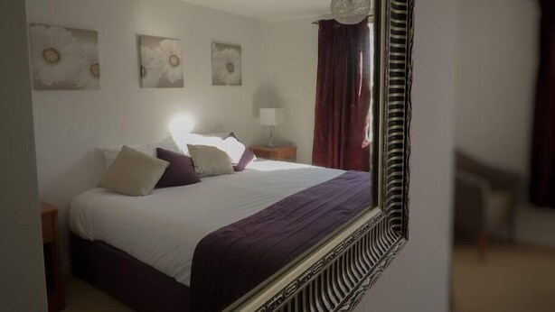 A bedroom with a large bed, a bedside table with a lamp, and a mirror reflecting the room.