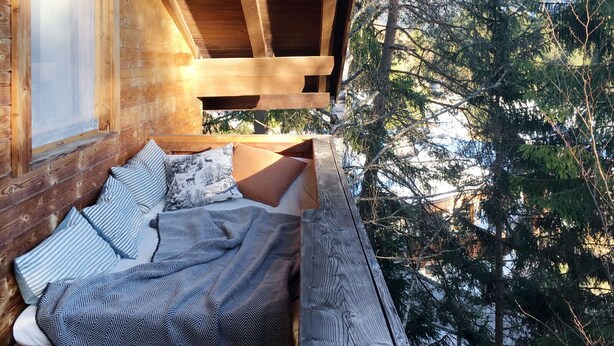 A cozy wooden cabin with a bed featuring striped and patterned bedding, a window, and a view of surrounding trees. - Waldhaus Neuleutasch, plenty of space to be outside, far away from the hustle and bustle (Leutasch)