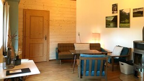 A cozy living room with a wooden floor, a sofa, a chair, a table with a vase, and a fireplace. - Waldhaus Neuleutasch, plenty of space to be outside, far away from the hustle and bustle (Leutasch)