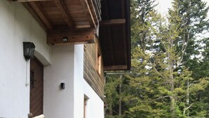 A white building with a wooden porch, a stone wall, and a garden with pink flowers. - Waldhaus Neuleutasch, plenty of space to be outside, far away from the hustle and bustle (Leutasch)
