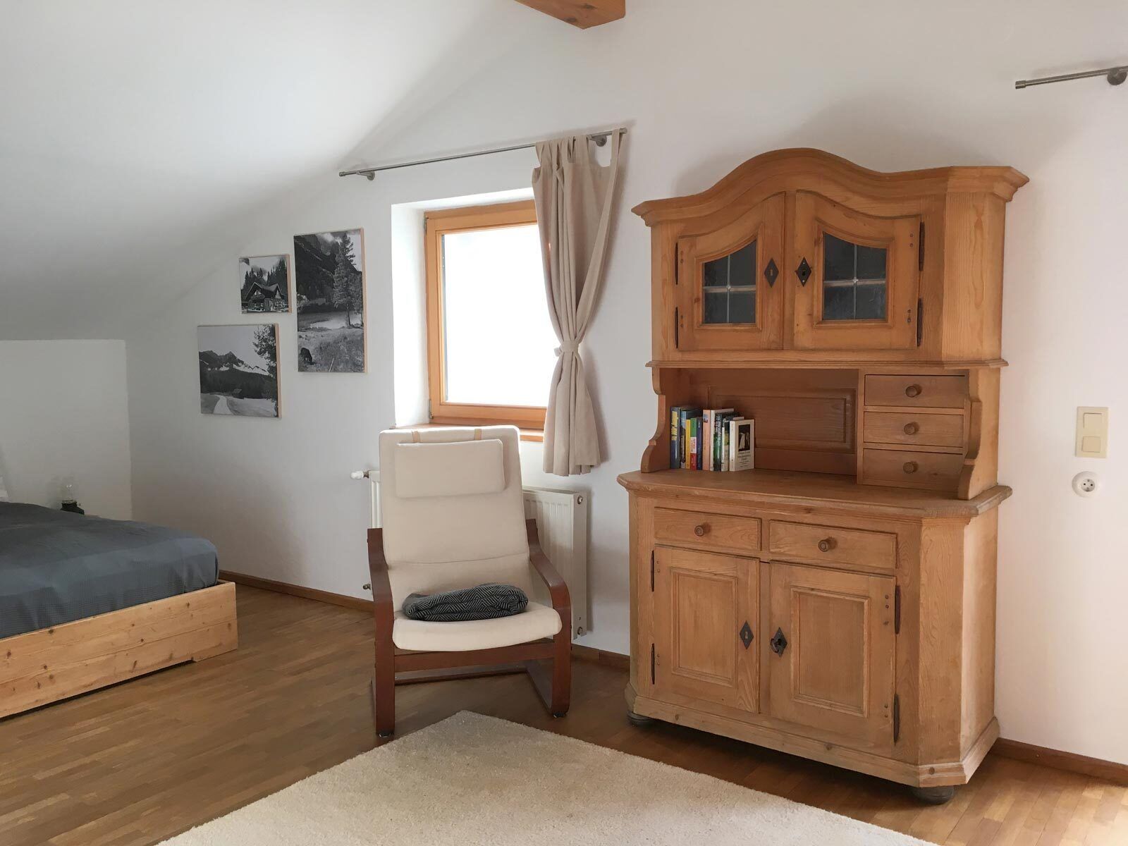 A bedroom with a wooden bed, a chair, a wooden dresser, and a window with curtains.