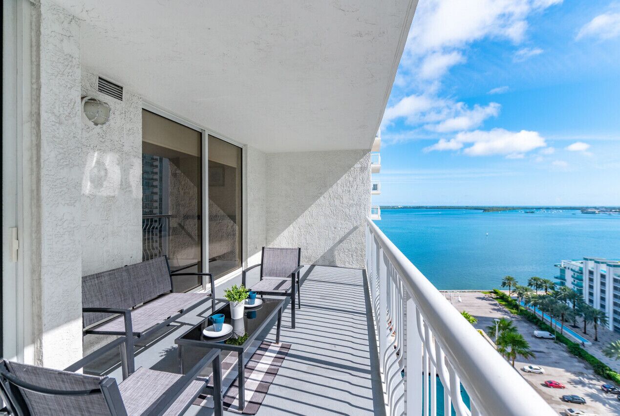 A balcony with a table and chairs, overlooking a body of water and a cityscape.