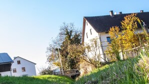 A narrow water channel with grass and reeds, flanked by buildings with white walls and dark roofs, under a clear blue sky. - Bauernhaus am Sallingbach (Rohr in Niederbayern)