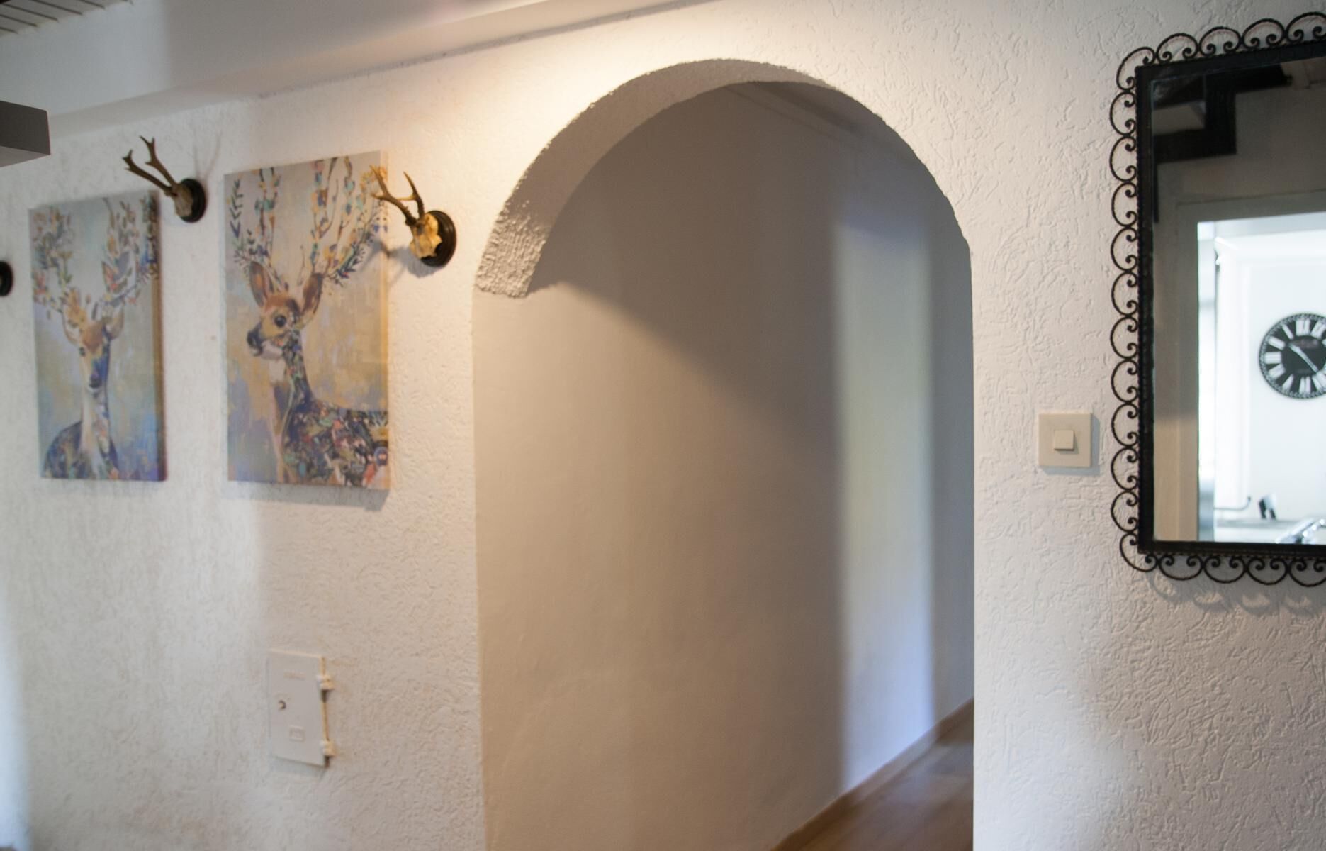 An interior hallway with a white wall, a decorative archway, and two framed paintings.