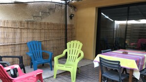 Eine Terrasse im Freien mit Plastikstühlen und einem Tisch, einer Bambuswand und einer Glastür.