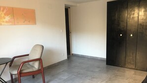 Ein geräumiges Zimmer mit einer großen, dunklen Holztür, einem beige farbenen Sessel und einem kleinen runden Tisch.