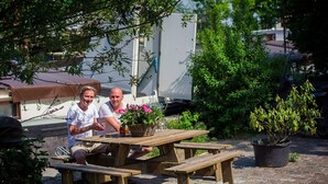 Een houten picknicktafel met bankjes, omringd door potplanten en een gebouw op de achtergrond.
