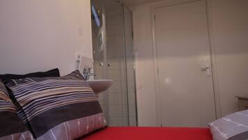 A bedroom with a red bedspread, a white door, and a shower area.