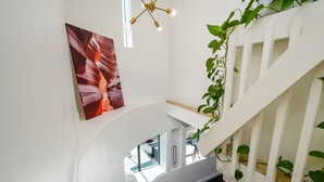 A modern staircase with a glass railing, a painting of red rock formations, and a hanging light fixture.