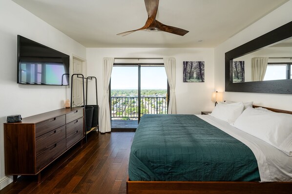 A bedroom with a bed, a dresser, a ceiling fan, a large window with curtains, and a balcony with a view of the city. - 270° City/Mountain views! (Phoenix)