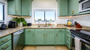 A modern kitchen with green cabinets, a stainless steel dishwasher, a built-in oven, and a large window offering a city view.