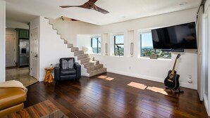 A spacious living room with a staircase, a mounted TV, and a guitar.