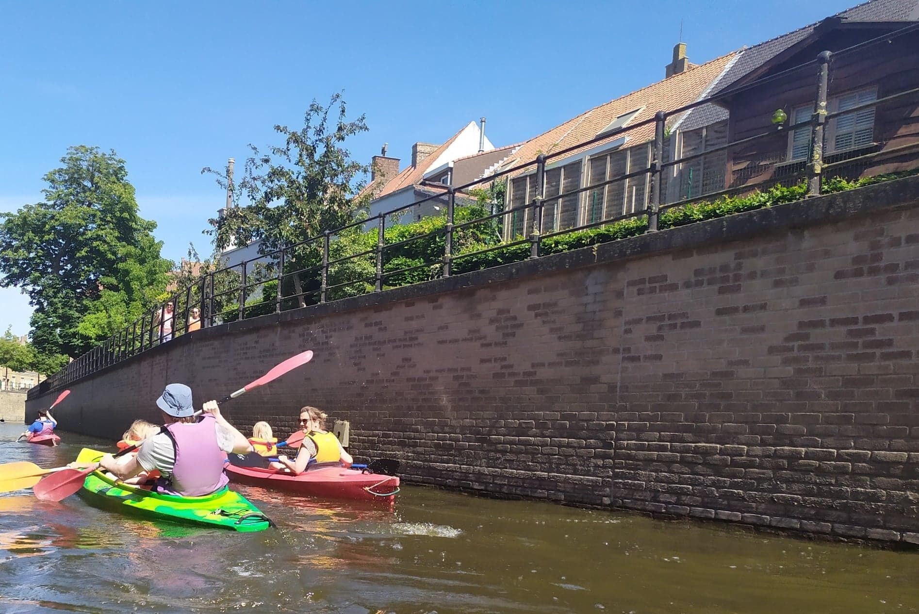 Un étroit canal où l’on peut faire du kayak, un mur de briques et des bâtiments en arrière-plan.