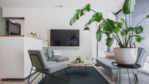 Un saló modern amb televisió de pantalla plana, dos butaques grises, una taula de centre i una planta gran en test.