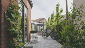 Un camí de maó estret amb una bicicleta i una taula amb caires, que condueix a l'entrada d'un edifici.