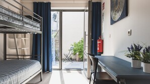 Una habitació de dormitori amb lliteres, escriptori, cadira i una planta en test.