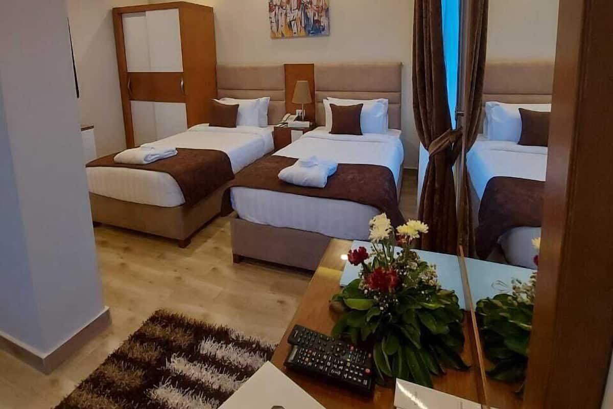 A hotel room with two beds, a desk with a remote control, a mirror, and a painting on the wall.