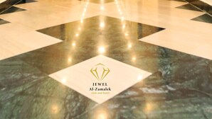 Un pasillo de hotel con piso de mármol pulido, sillas de madera y plantas en macetas.