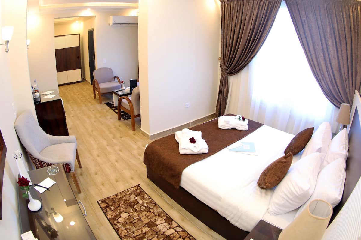 A hotel room with a bed, a desk, a chair, a mirror, and a window with curtains.
