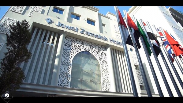 L’extérieur de l’hôtel juif Zamatek présente une architecture moderne, avec une grande fenêtre en arc d’un style remarquable et une série de drapeaux.