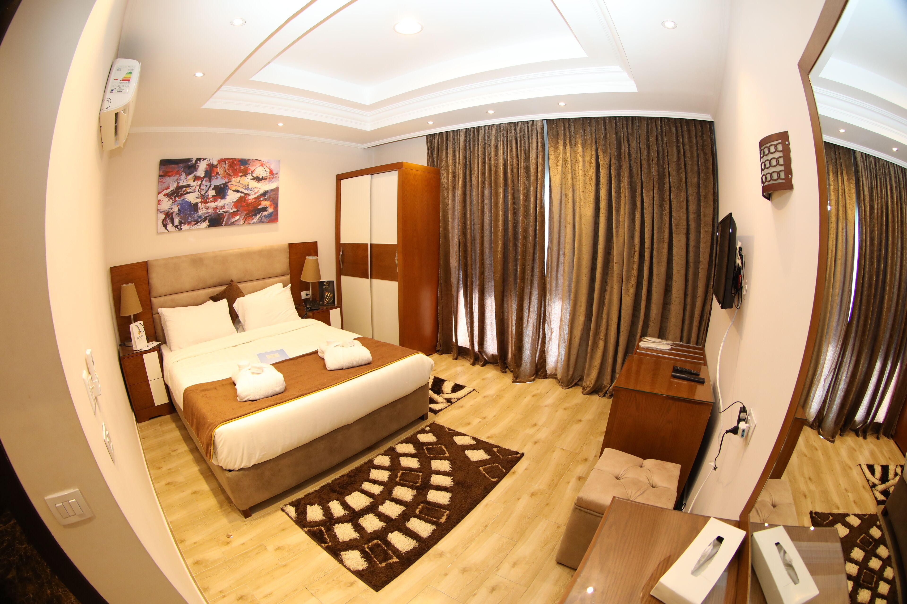 A hotel room with a large bed, a desk, a chair, a TV, and a window with curtains.
