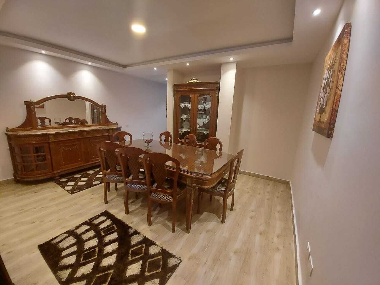 A dining area with a wooden table and chairs, a cabinet, and a patterned rug.