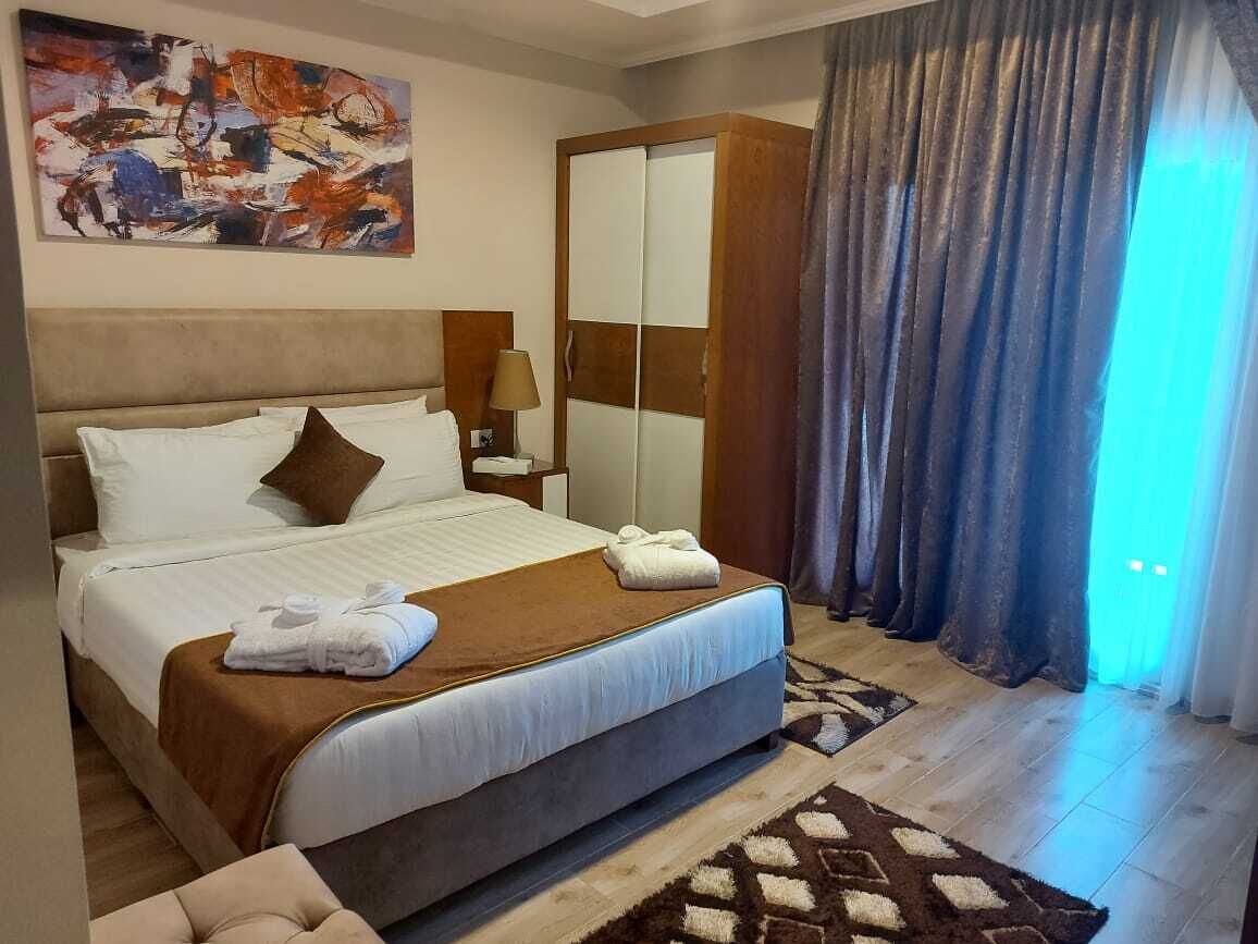 A hotel room with a large bed, a wardrobe, a nightstand, and a painting on the wall.
