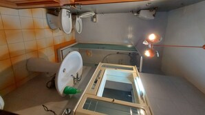 Pieni kylpyhuone, jossa on wc, bidee ja pesuallas. Kylpyhuoneessa on puinen ovi ja peili, joka on sijoitettu pesualtaan yläpuolelle.