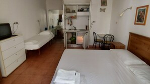 Hotellihuone, jossa on sänky, työpöytä, tuoli, lipasto ja pieni keittiö.