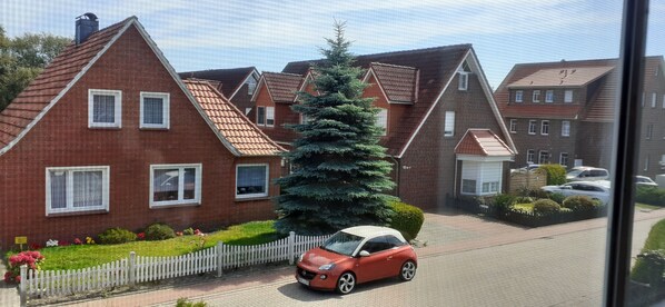 Une rue résidentielle bordée de maisons en briques, une voiture rouge garée sur le côté et une clôture blanche en bois.