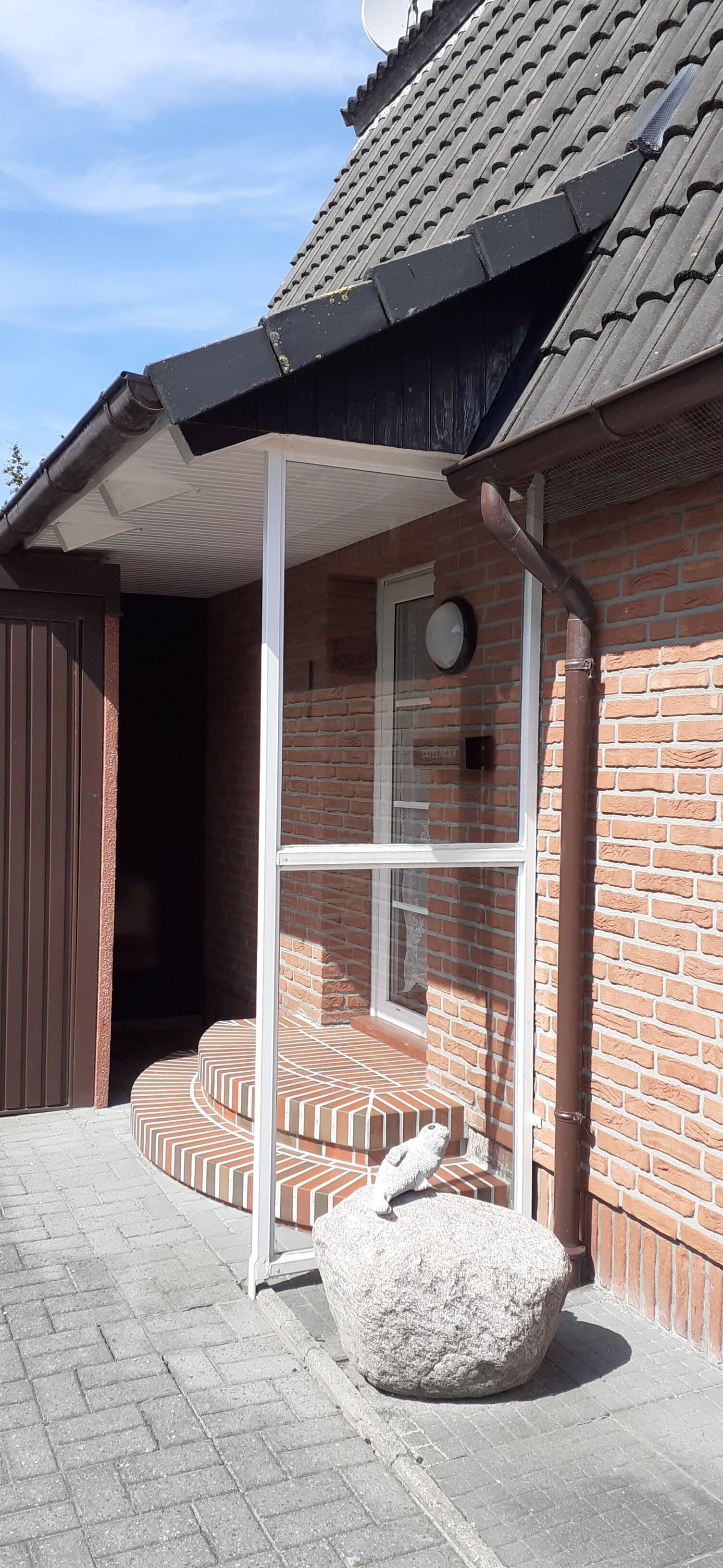 Een gebouw van baksteen met een pannendak, een glazen deur en een stenen bank ervoor.