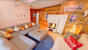 Un salón moderno con un sofá seccional, una chimenea, paredes de madera y un diseño geométrico en la pared.