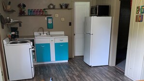 Una cocina compacta con electrodomésticos blancos, armarios azules y un microondas sobre el refrigerador.