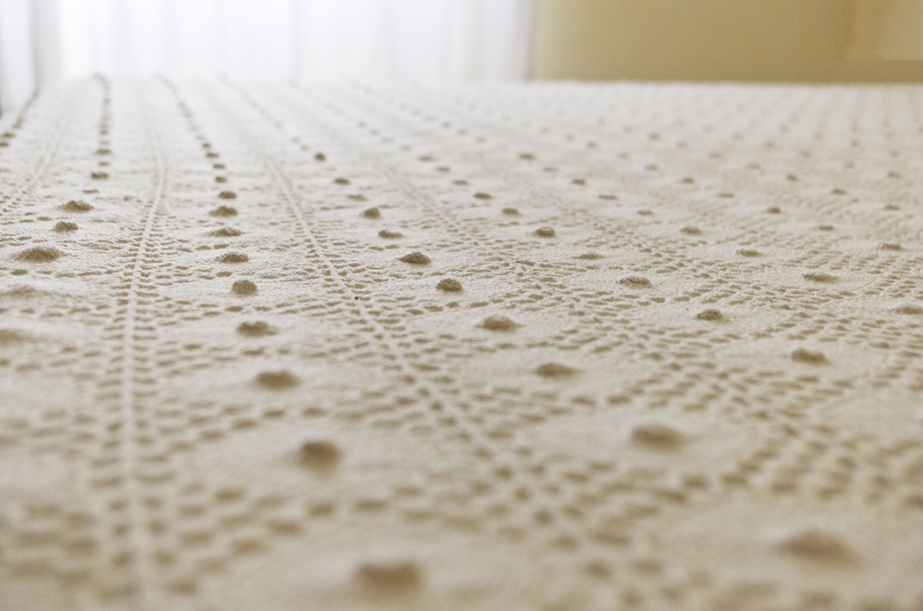 A close-up of a textured fabric, possibly a bedspread or tablecloth, with a detailed pattern.