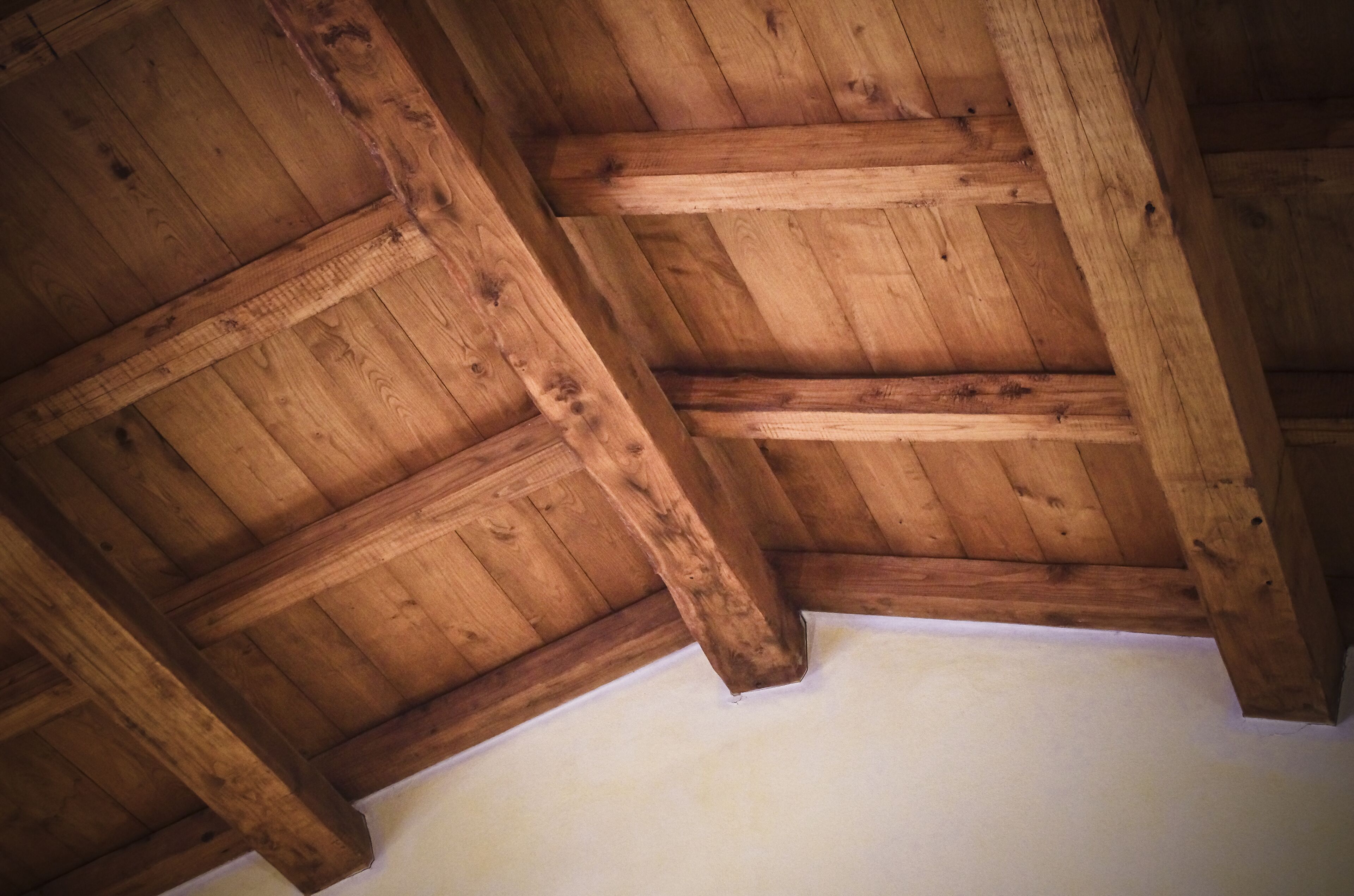 Een houten plafond met zichtbare balken en een witte muur.