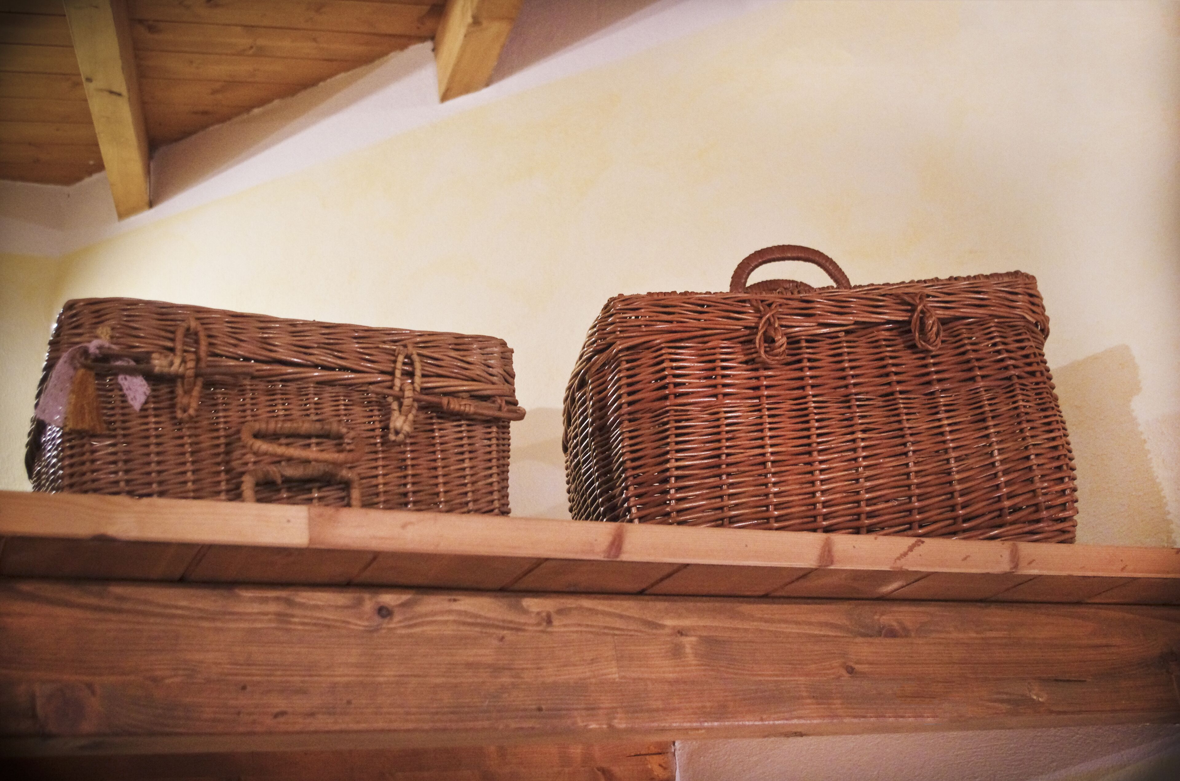 Two wicker baskets on a wooden shelf against a plain wall.