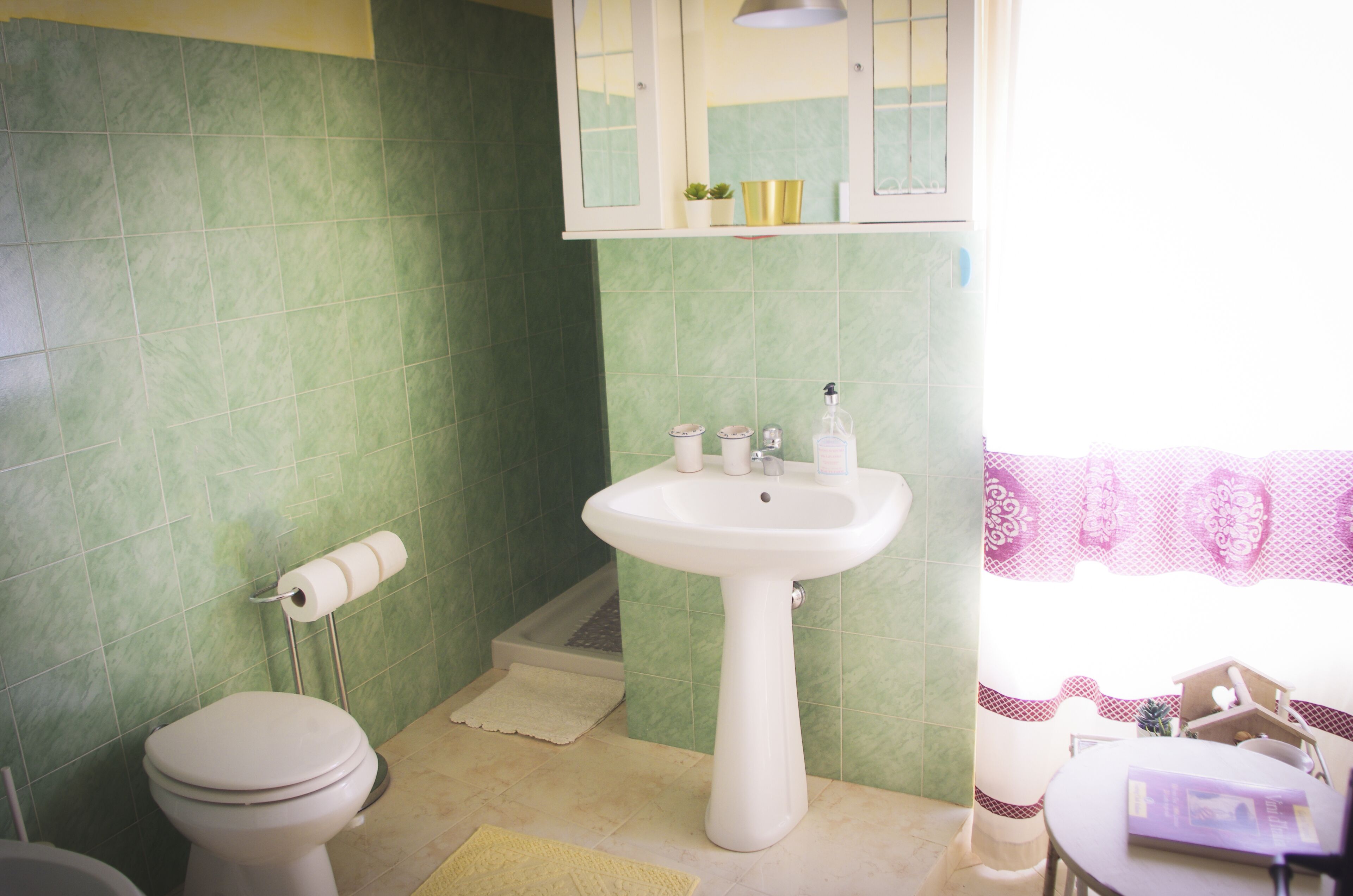 A bathroom with a toilet, sink, and green tiled walls.