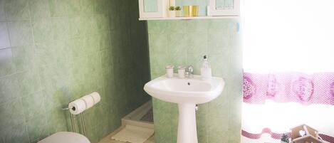 A bathroom with a toilet, sink, and green tiled walls.