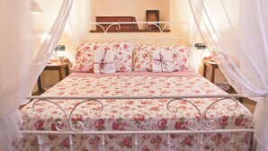 Una cama con colcha y almohadas estampadas, una mesita de noche con lámpara y una mesita auxiliar con reloj.