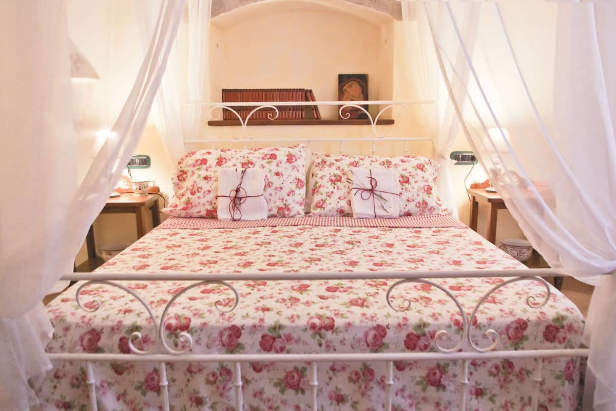 A bed with a floral bedspread and matching pillows, a bedside table with a lamp, and a nightstand with a clock.
