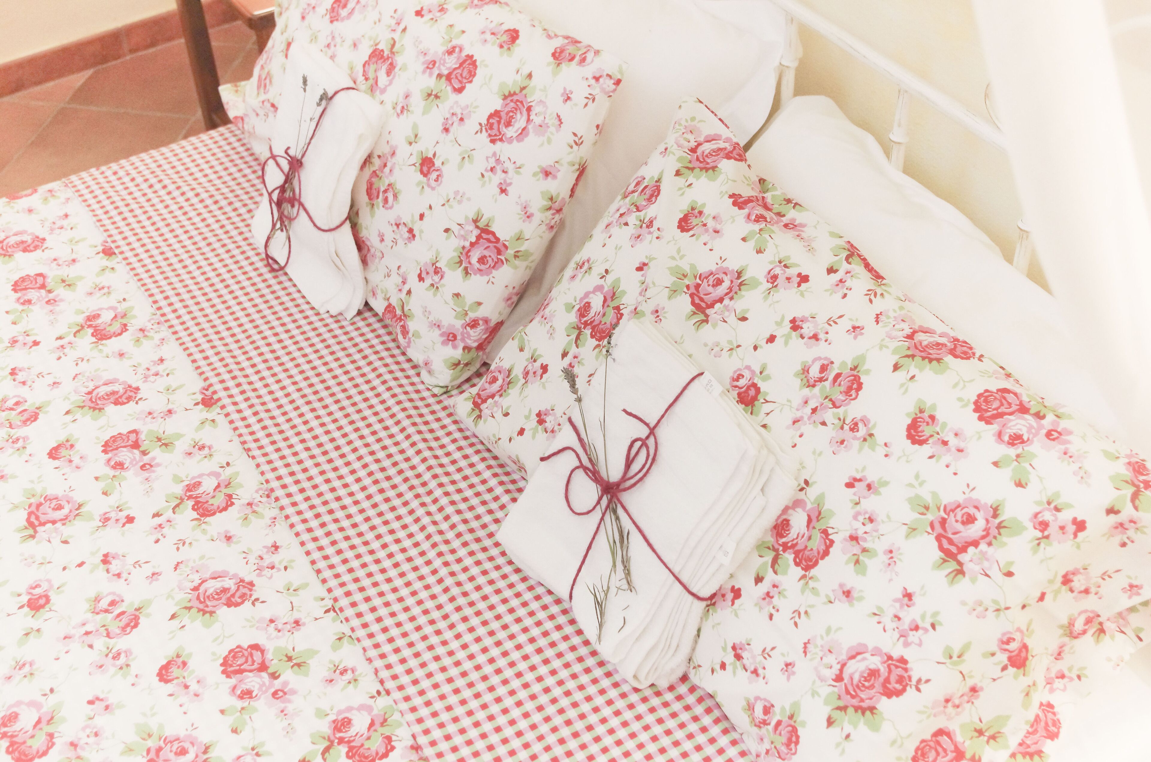 Una cama bien hecha con ropa de cama floral y una funda de almohada a cuadros.