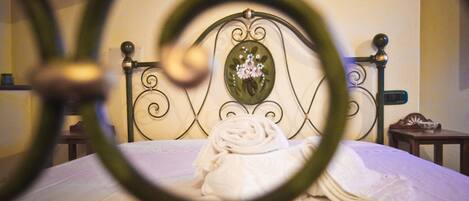 Un lit bien fait, agrémenté d’une tête de lit décorative, une table de chevet avec une lampe et une petite étagère sur laquelle se trouve un bol.