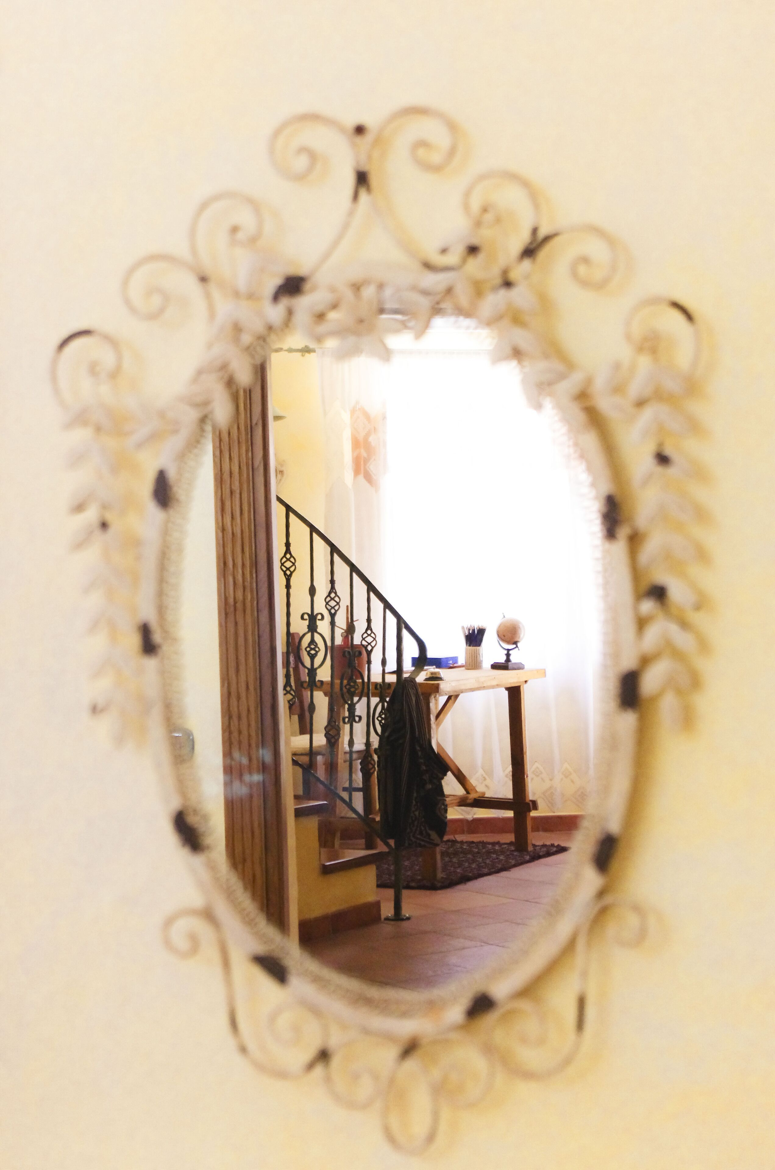 Uno specchio con cornice decorativa che riflette una scala, un tavolo con un vaso e una sedia.