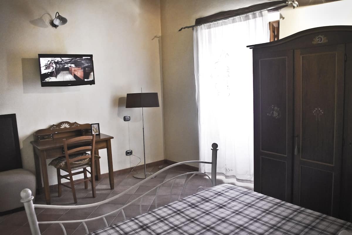 A bedroom with a bed, a desk, a chair, a wardrobe, a television, and a lamp.