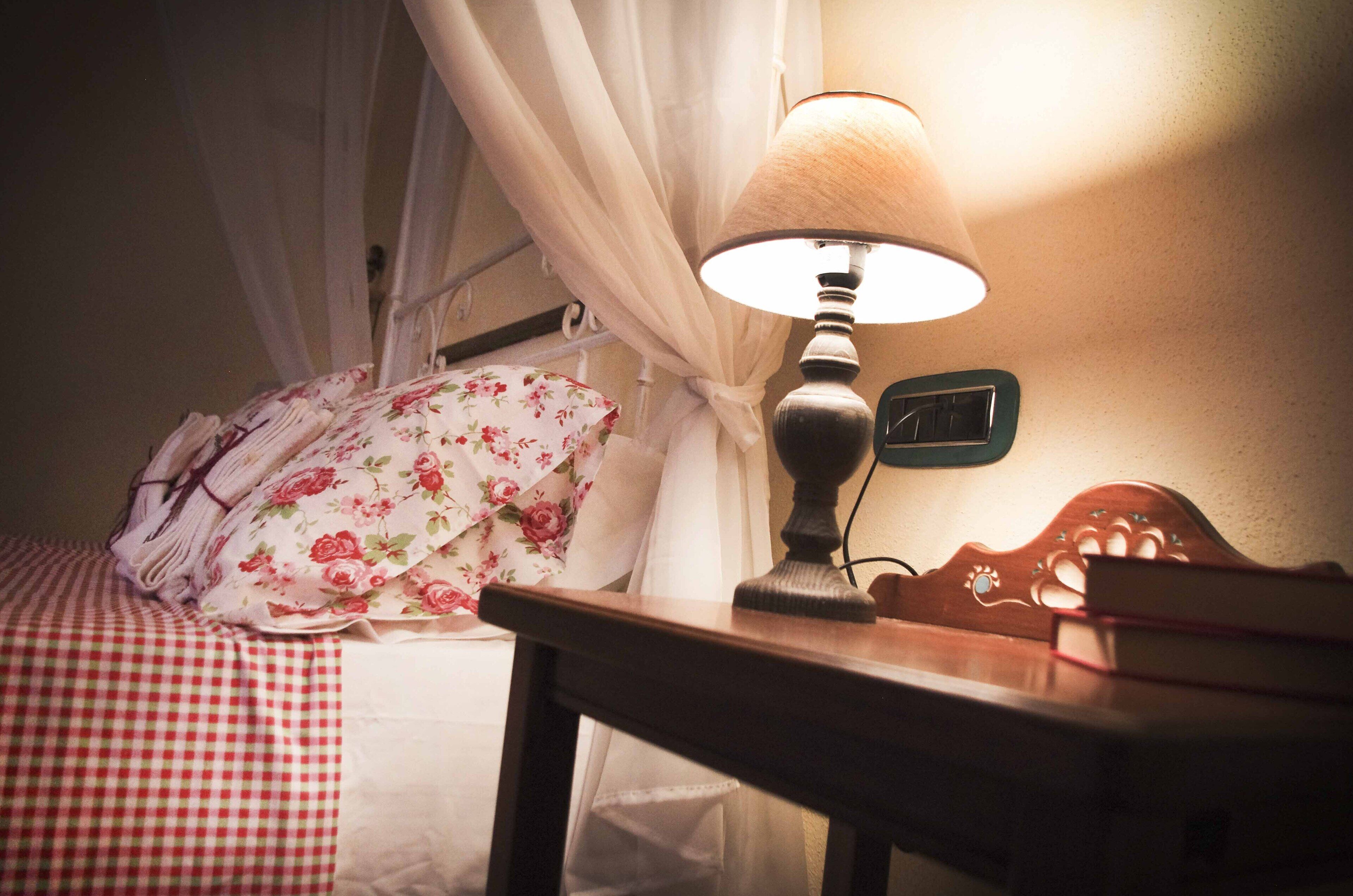 A bed with floral bedding, a bedside table with a lamp, and a wall clock.