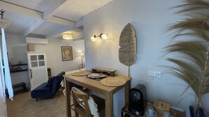 Una sala acogedora con una mesa de centro de madera, un sofá y una mesa de comedor con individuales. Hay una lámpara de pared y una hoja decorativa en la pared.